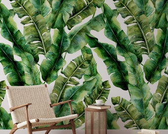 May include: A white wall with a green and white tropical banana leaf wallpaper. A woven wicker chair and a small woven wicker side table with a book on top are in front of the wall.