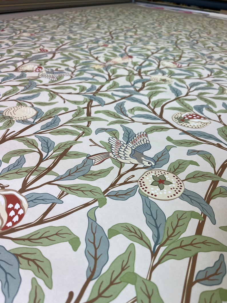 May include: A vintage wallpaper design featuring a repeating pattern of stylised trees, birds, and pomegranates. The wallpaper is cream-coloured with brown branches, green and blue leaves, and red and white pomegranates.