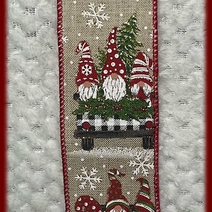 May include: Decorative ribbon featuring gnomes in red hats riding in a truck bed filled with greenery and a buffalo plaid pattern. Snowflakes and the text "Maine Balsam Wreaths" are also present.