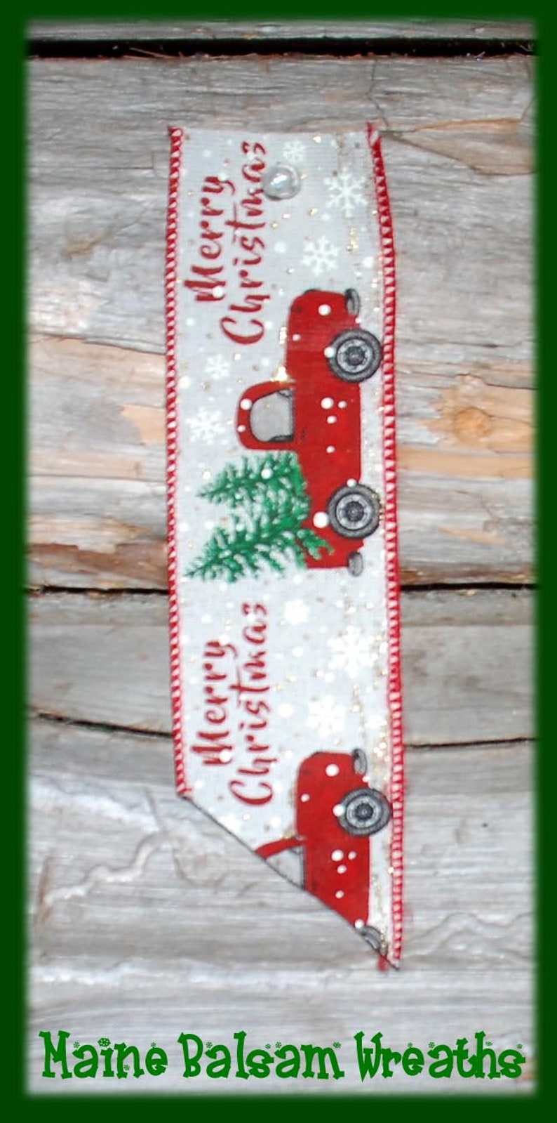 May include: A Christmas-themed ribbon with a red truck carrying a Christmas tree. The ribbon has the words "Merry Christmas" and snowflakes on a white background. The edges are red.
