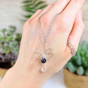 May include: A silver chain necklace with a silver wire lotus flower pendant and a black lava rock bead and a clear crystal bead.