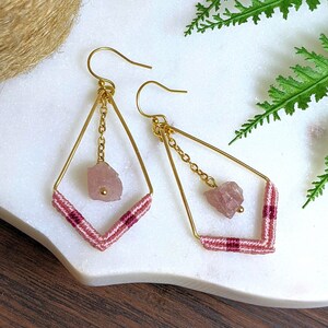 May include: Gold geometric earrings with pink and red thread and a pink stone pendant.