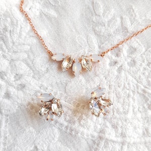 May include: A rose gold necklace and matching stud earrings set featuring marquise-cut clear crystals and opaque white stones arranged in a cluster design. The necklace has a delicate rose gold chain, and the earrings mirror the necklace's cluster.
