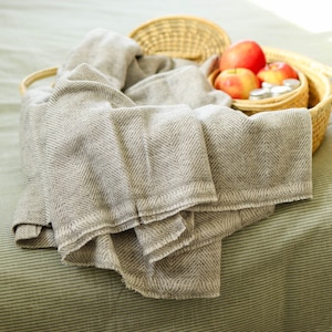 May include: A gray and white herringbone throw blanket draped over a wicker basket filled with red apples and glass jars.