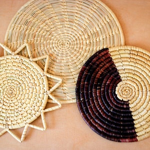 May include: Three woven straw placemats, one with a sunburst design, one with a solid circular design, and one with a half-circle design in brown and natural straw.