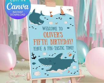 Puede incluir: Un letrero de cumpleaños azul claro sobre un caballete con ilustraciones de tiburones y el texto "WELCOME TO OLIVER'S FIFTH BIRTHDAY! HAVE A FIN-TASTIC TIME!". El letrero está rodeado de decoraciones y globos rosas y azules.