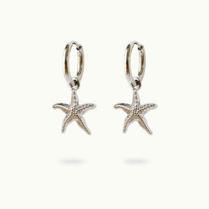May include: A pair of silver-colored hoop earrings, each featuring a starfish charm. The starfish charms have a textured surface and are suspended from the bottom of the hoops. The earrings are displayed against a white background.