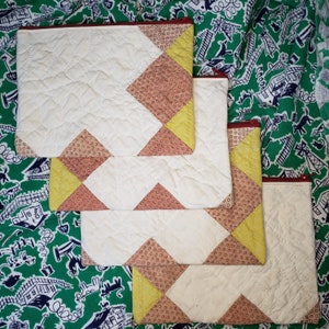 May include: Three quilted fabric zipper pouches with a patchwork design. The pouches are white with pink and yellow geometric patterns.