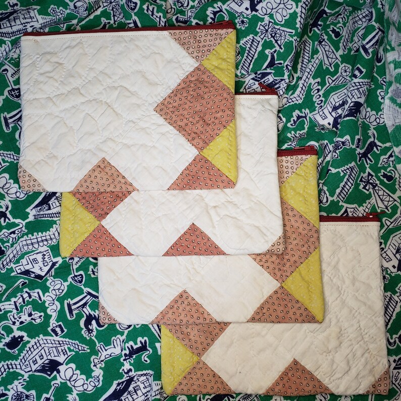 May include: Three quilted fabric zipper pouches with a patchwork design. The pouches are white with pink and yellow geometric patterns.