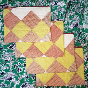 May include: Four quilted fabric pouches with a diamond pattern in shades of yellow, orange, and white. The pouches are stacked on top of each other.