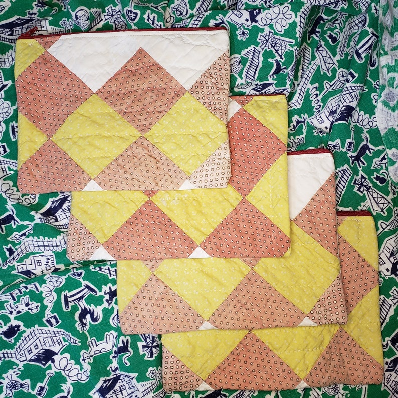 May include: Four quilted fabric pouches with a diamond pattern in shades of yellow, orange, and white. The pouches are stacked on top of each other.