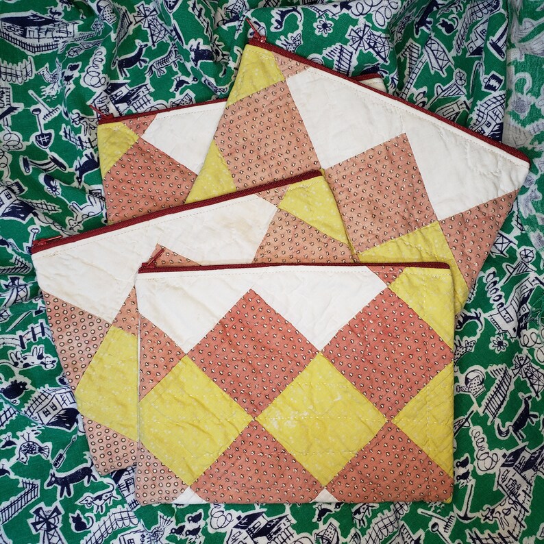 May include: Three quilted zipper pouches with a patchwork design. The pouches are made of white, yellow, and pink fabric with a small polka dot pattern. The pouches are stacked on top of each other.