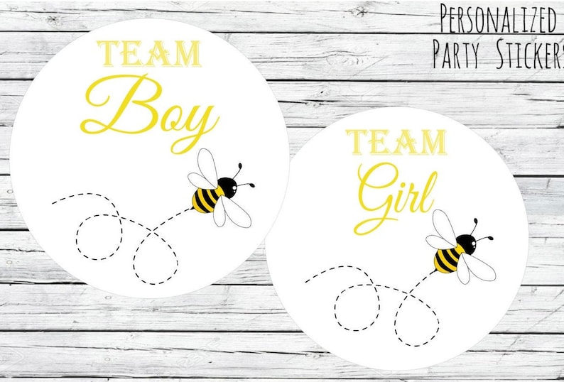 K&ouml;nnte beinhalten: Zwei runde wei&szlig;e Aufkleber mit schwarzen Umrissen. Die Aufkleber zeigen eine gelbe Biene mit schwarzen Streifen, die mit einer gepunkteten Linie dahinter fliegt. Der Text "Team Boy" und "Team Girl" ist in gelber Kursivschrift auf den Aufklebern geschrieben.