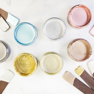 May include: Eight small jars of metallic paint in various colors, including silver, gold, light blue, light pink, and beige. Each jar has a small wooden stick with a dab of paint on the end.