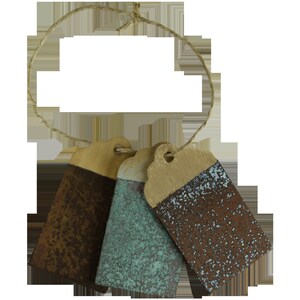 May include: Three small, rectangular, brown paper tags with a string attached. The tags are painted with a speckled, multi-coloured paint effect. The colours are brown, blue, and green.