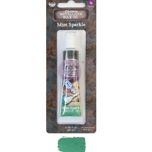 May include: A tube of Mint Sparkle Metallic Wax by Art Alchemy. The tube is green and has a white cap. The label is brown with white text. The text on the label reads "Art Alchemy Metallic Wax Cire Cera" and "Mint Sparkle".