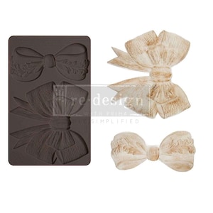 May include: A silicone mold for making three different bow shapes. The mold is dark brown and the bows are shown in a light brown color.