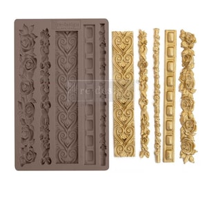May include: A brown silicone mold with various decorative border designs, including roses, hearts, and geometric patterns. Several gold-colored resin castings of the same designs are displayed next to the mold. The mold has the text "re-design with prima".