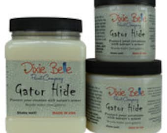 May include: Three jars of Dixie Belle Paint Company Gator Hide paint. The jars are white with a green label and the text "Gator Hide" in black. The largest jar is 32 oz, the middle jar is 16 oz, and the smallest jar is 8 oz.