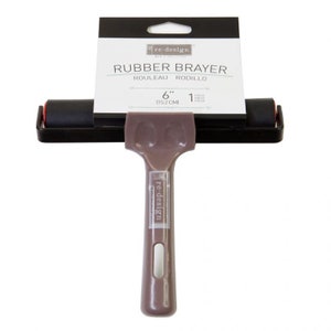 May include: A 6-inch (15.2 cm) black rubber brayer with a brown plastic handle. The handle has the text "re-design" printed on it. The brayer is packaged in a clear plastic bag with a white label that says "RUBBER BRAYER" and "ROULEAU RODILLO".