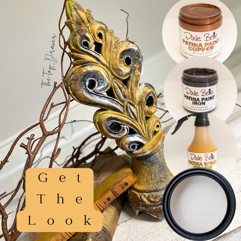 May include: A decorative metal ornament with a gold and black finish, styled with a distressed look. The ornament is displayed on a book with a wooden surface. Three bottles of Dixie Belle Patina Paint are shown in the image: Copper, Iron, and a spray bottle of Patina.
