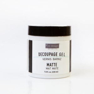 May include: A white jar with a black lid and label. The label reads "re-design Decoupage Gel Vernis Barniz Matte Mat Mate 7.8 fl. oz. (230 ml)"