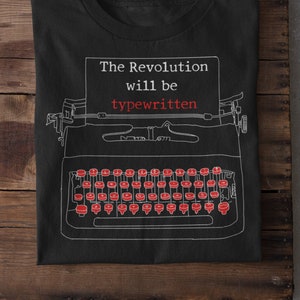 May include: Black t-shirt with a white outline of a typewriter and the text "The Revolution will be typewritten" in red.