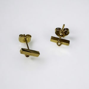 Peut inclure: Une paire de boucles d'oreilles clous en forme de barre dorées. Les boucles d'oreilles sont simples et minimalistes, avec un design de barre droite.