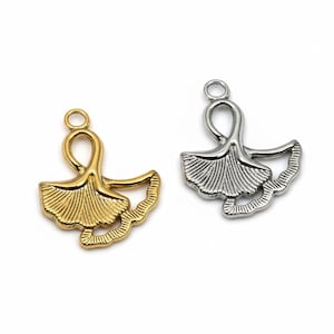 Könnte beinhalten: Zwei Metallanhänger in Form von Ginkgoblättern. Einer ist goldfarben, der andere silberfarben. Jeder Anhänger hat ein detailliertes Blattdesign mit einer Schlaufe oben zum Befestigen an Schmuck oder anderen Bastelarbeiten. Die Anhänger sind vor weißem Hintergrund.
