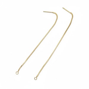 May include: A pair of delicate gold-colored chain earrings. Each earring features a post for insertion and a long, slender chain that dangles down. The chains are made of small, square links and have a small loop at the end.