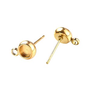 Op de afbeelding: Twee goudkleurige oorbelpalen met een ronde, bekerachtige setting en een kleine lus. De palen hebben een eenvoudig, recht ontwerp en de settings zijn ontworpen om een steen of ander decoratief element vast te houden. De oorbellen worden tegen een witte achtergrond getoond.