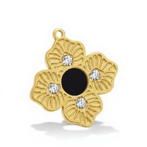 Op de afbeelding: Een goudkleurige bloemhanger met vier bloemblaadjes, elk met een textuurontwerp. Het midden van de bloem is zwart en elk bloemblad heeft een sprankelende, heldere edelsteen. De hanger heeft een kleine lus aan de bovenkant voor een ketting.