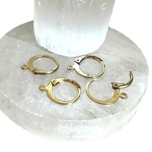 Peut inclure: Cinq créoles d'oreille dorées avec une fermeture à charnière. Les créoles sont disposées sur une surface blanche.