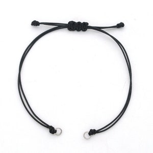 Peut inclure: Un bracelet ajustable simple noir avec des anneaux en métal argenté aux extrémités.