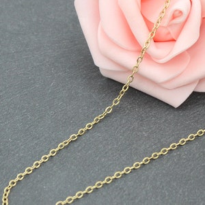 Könnte beinhalten: Eine goldene Kettenkette auf einem grauen Hintergrund mit einer rosa Rose.