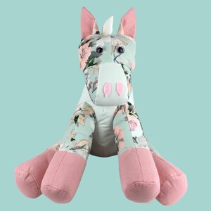 May include: A plush toy unicorn with a floral print fabric in shades of blue, green, and pink. The unicorn has pink ears, a white horn, and pink hooves.