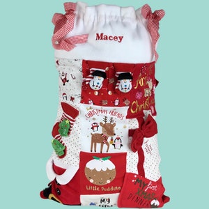 May include: A personalised Christmas stocking with a white top and red and white patchwork fabric. The stocking is decorated with various Christmas-themed designs, including a snowman, reindeer, penguins, and a Christmas pudding. The stocking is personalised with the name "Macey".