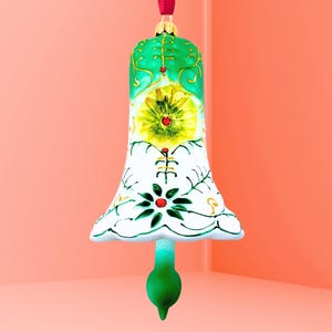 May include: A decorative glass bell ornament with a red ribbon for hanging. The bell is painted with green, white, and yellow floral designs. The bell's base is a darker green, and the top is a lighter green.