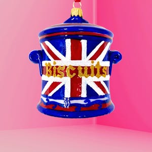 Pode incluir: Enfeite de pote de biscoitos azul e vermelho com um design da bandeira britânica. A palavra "Biscuits" está escrita em glitter dourado. Inclui uma fita vermelha para pendurar.