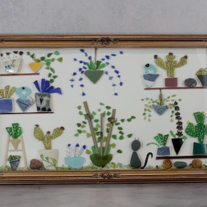 May include: A framed artwork featuring a collection of glass mosaic plants and a cat. The plants include cacti, hanging plants, and potted flowers in various colors. The frame is gold-toned with ornate detailing, creating a decorative piece.