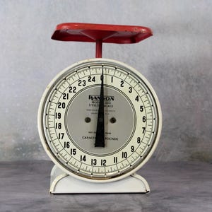 May include: A vintage Hanson Model 2000 utility scale with a white circular body and a red metal weighing platform. The dial features black numbers from 0 to 24, a black needle, and text reading Hanson Model 2000 Utility Scale, Capacity 25 Pounds.