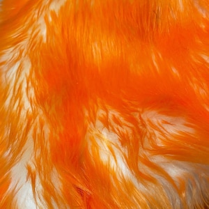 May include: Close-up of a fluffy orange and white faux fur fabric. The fur is soft and plush, with a subtle ombre effect.