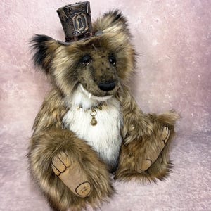 May include: A plush bear with brown and white fur, wearing a dark brown top hat featuring a keyhole design. The bear has a spiked collar with a small bell, visible fangs, and tan paw pads with the name Jai inscribed on the bottom of one foot.