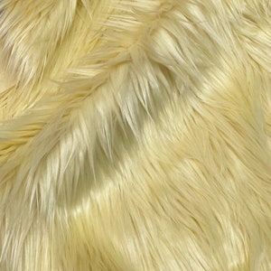 May include: A close-up of a soft, pale yellow faux fur fabric. The fur is long and fluffy, creating a luxurious and cosy texture.