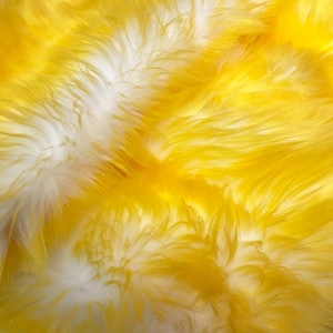 May include: A close-up of a yellow and white faux fur fabric. The fur is soft and fluffy, with a gradient of colour from yellow to white.