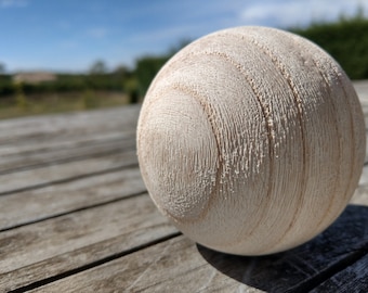 May include: A close-up of a white wooden ball with a textured surface. The ball is sitting on a wooden table.