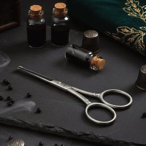 Może przedstawiać: Asortyment artykułów aptecznych na ciemnej powierzchni. Obejmuje małe szklane butelki z korkami, parę srebrnych nożyczek i naparstki. Butelki są wypełnione ciemnym płynem, a małe czarne koraliki są rozrzucone.