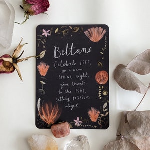 Pu&ograve; includere: Carta nera con un disegno floreale e il testo "Beltane Celebrate LIFE, on a warm SPRING night, give thanks to the FIRE, setting PASSIONS alight."