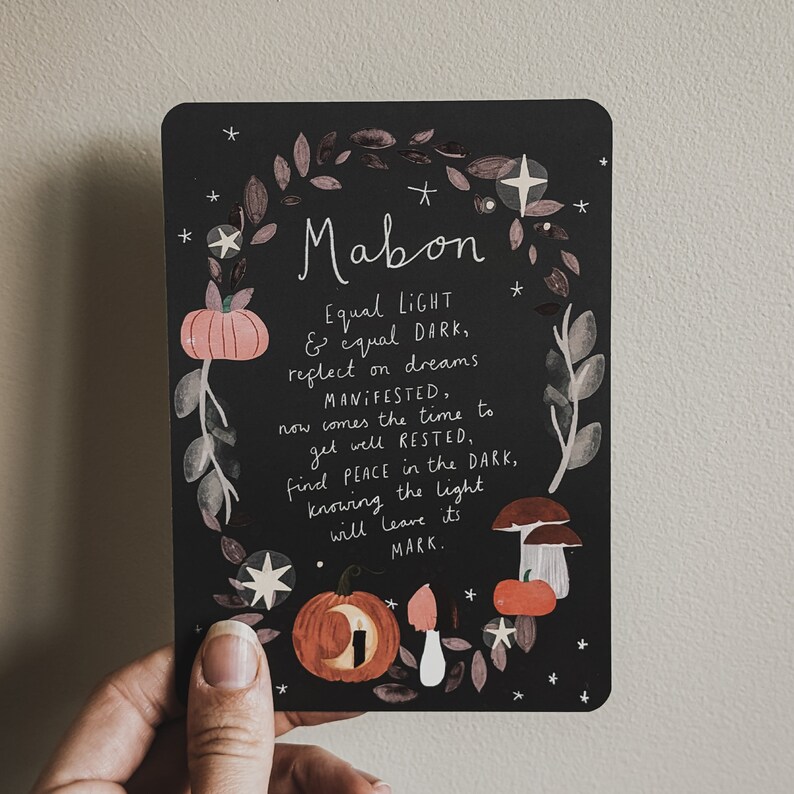 May include: A black card with a white illustration of a pumpkin, leaves, and stars. The text on the card reads "Mabon Equal LIGHT & equal DARK, reflect on dreams MANIFESTED, now comes the time to get well RESTED, find PEACE in the DARK, knowing the light will leave its MARK."