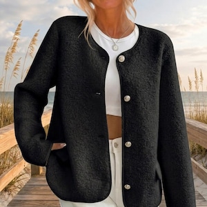 May include: A black textured long-sleeve jacket with a round neckline and four silver-toned buttons down the front. The jacket is worn over a plain white t-shirt. The fabric has a fuzzy, fleece-like appearance with a consistent dark black color.